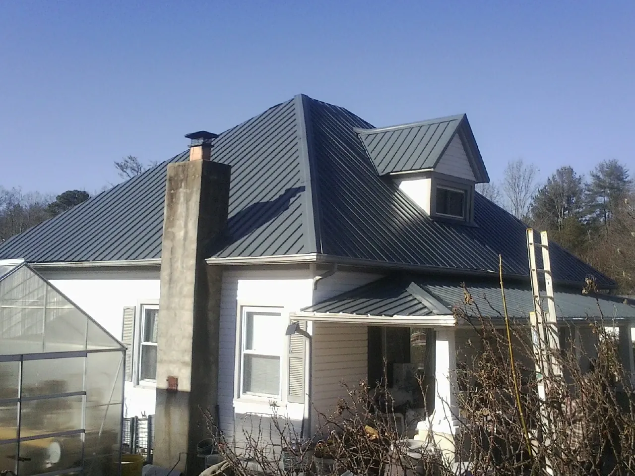 Dark blue standing seam metal roof on a white farmhouse with dormer — Slate & Tile Roof Repair by Roofing Brothers in Hodges