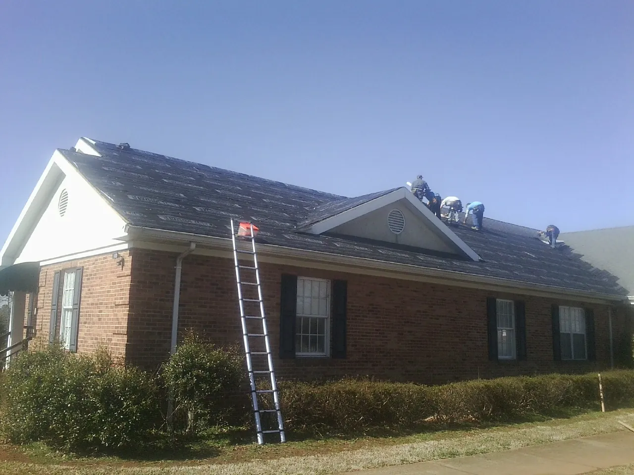 Crew tearing shingles off a brick ranch roof with a ladder set — Emergency Roof Repair work by our crew in Hodges