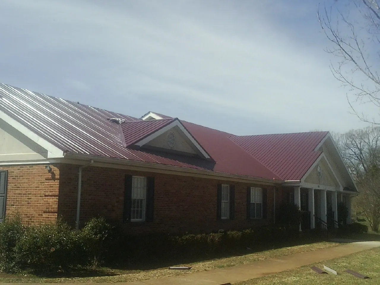 Red metal roof with gabled entries on a long brick building, from a Hail Damage Roof Repair job in Hodges