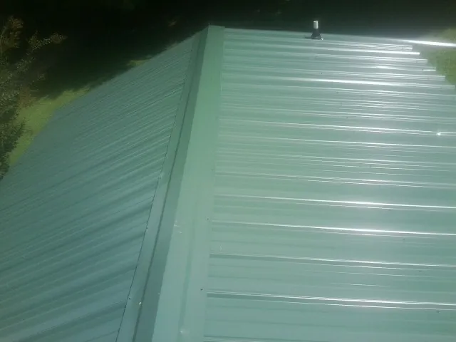 New green metal panels meeting at the ridge of a roof — Flat Roof Repair work by our crew in Hodges