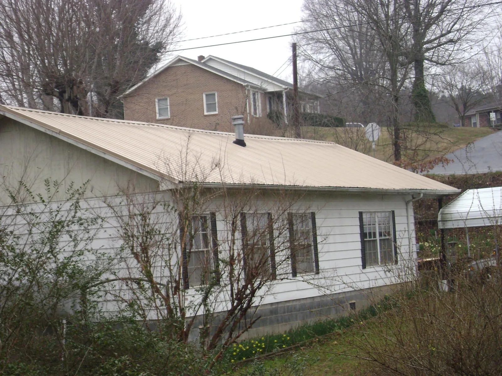 Tan metal roof on a white sided house set into a hillside — Commercial Roofing by Roofing Brothers in Hodges