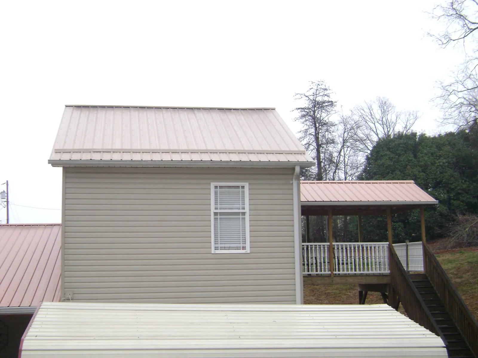 Tan metal roofs on a two story addition and attached porch, from a Roof Replacement job in Hodges